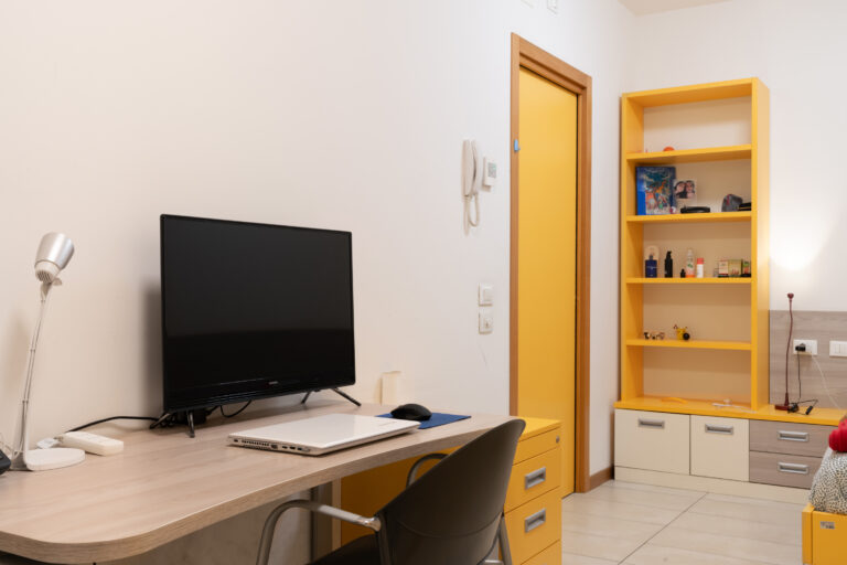 Alloggio della Residenza Colombo con un letto, uno scaffale e una scrivania
